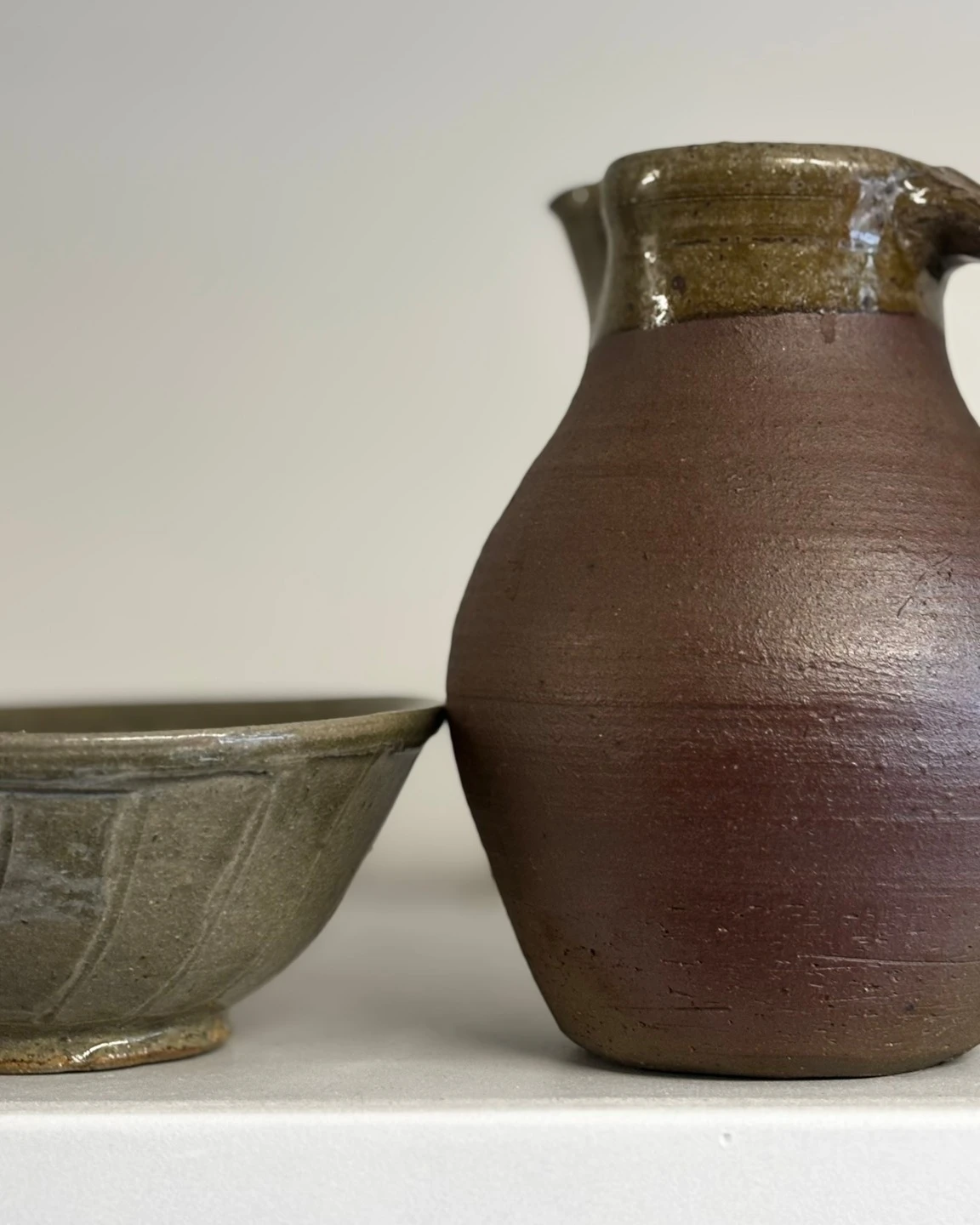 Brown ceramic jug and green glazed bowl on a white shelf at Cleo's